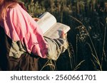 Christian girl holds bible in her hands. Reading the Holy Bible in a field during beautiful sunset. Concept for faith, spirituality and religion.