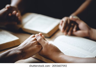 Christian group of people holding hands praying worship to believe and Bible on a wooden table for devotional or prayer meeting concept.