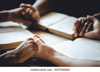 Christian Group Of People Holding Hands Praying Worship To Believe And Bible On A Wooden Table For Devotional Or Prayer Meeting Concept.