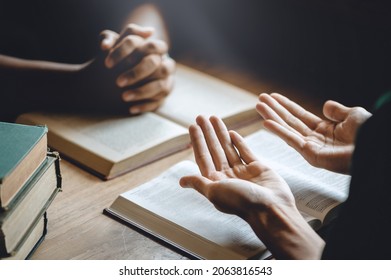 Christian Group Of People Holding Hands Praying Worship To Believe And Bible On A Wooden Table For Devotional Or Prayer Meeting Concept.
