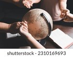 Christian group praying for globe and people around the world on wooden table with bible. Christian small group holding hands and praying together around a wooden table with bible page in homeroom.