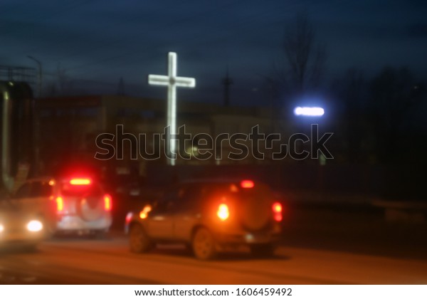 Christian, a large cross with white LED\
backlight on a highway with vehicles under a blue, summer sky. \
Night blurred\
background