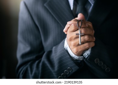 Christian Man In A Suit Praying With A Cross. Hands Close Up.