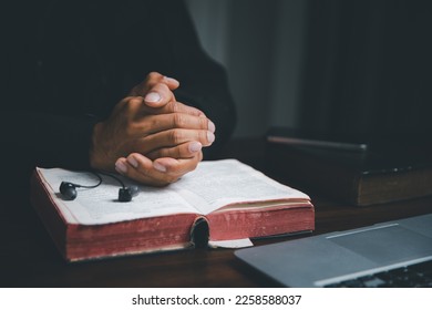 Christian online technology concept. Hands praying of christian with digital computer laptop, Online live church for sunday service. Asian catholic man are reading Holy bible book and online study.
