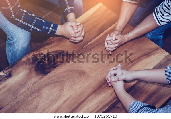 Christian people prays together around\
wooden table. prayer meeting small group\
concept.