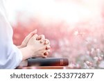 Christian praying and worshiping with both hands clasped on the holy bible, with a beautiful flower field in the background
