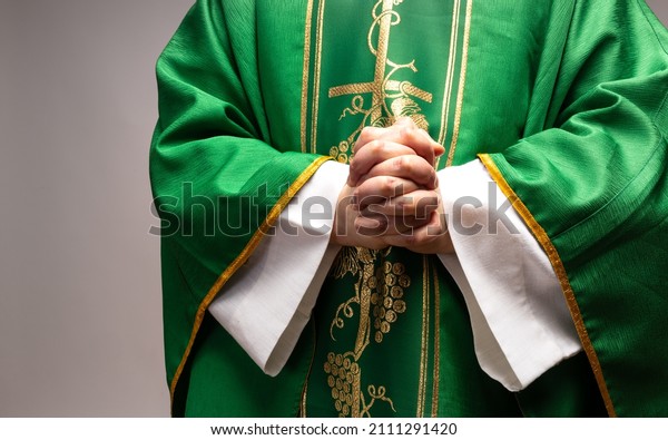 The Christian priest holds his hands folded. The\
priest wears liturgic\
clothes.