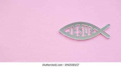 Christian sign of the fish. Gray fish with the word Jesus on a pink background, Christianity background with copy space