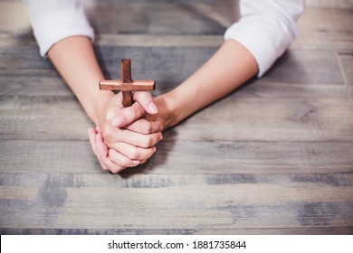 Christian Woman Doing Praying Hands And Holding Wooden Cross On Wood Table. Concept For Religious ,faith, Spiritual ,Peace, Hope 