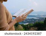 Christian woman holds a Bible in her hand Read the Bible on an island with a sea beach and many buildings. Concept for faith, spirituality and religion. peace hope