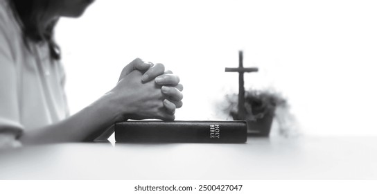 Christian woman praying and worshiping with her hands together in meditation, the cross of Jesus Christ and the Holy Bible
