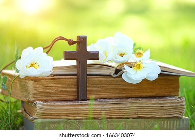 Christian wooden cross, rose flowers and old biblical books in garden, green sunny natural background. symbol of Easter, Orthodox palm Sunday. Christianity, Lent, Faith in God, Church holiday concept