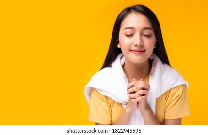 Christian Young Lady Praying To God. Woman Praying With Hands Together On Yellow Background. Attractive Girl Thank You For God Blessing To Wishing Have A Better Life. She Believe In Goodness, Hopeful