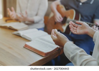 Christian young man group are playing guitar and sings a song from a Christian hymn book and the holy bible with his friends at home, Christian family worship or fellowship group concept
