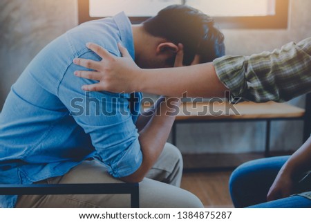 A Christian young man  praying for his friends while sitting on wooden chair at church prayer room to encourage and support him in his problem and spiritual growth.