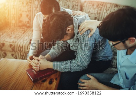 A Christian young man praying for his friends while sitting on a wooden chair at home to encourage and support him in his problem can be used for coronavirus crisis concept.