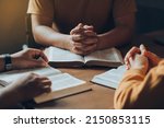 Christians and Bible study concept.Christian family sitting around a wooden table with open bible page and holding each other