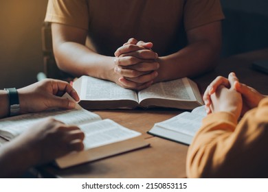 Christians and Bible study concept.Christian family sitting around a wooden table with open bible page and holding each other's hand praying together. - Shutterstock ID 2150853115