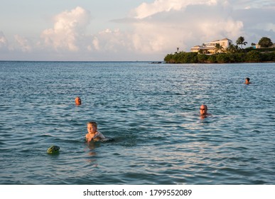 Christiansted, St. Croix, US Virgin Islands-June 15,2014: Group Of People At Southgate Beach During Sunset Playing Football In The Caribbean Sea With Coastal Home In Background In The US VI