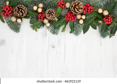 Christmas Abstract Background  Border With Flora Of Holly, Ivy, Gold Baubles And Pine Cones With Snow Covered Winter Greenery Over Distressed White Wood.