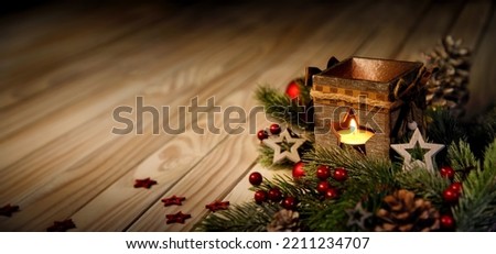 Christmas or advent background with a candle burning in a lantern on an elegant wooden surface, low key mood