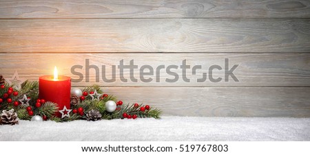 Christmas or Advent wood background with a burning candle on snow, decorated with fir branches and ornaments, panoramic format with copy space