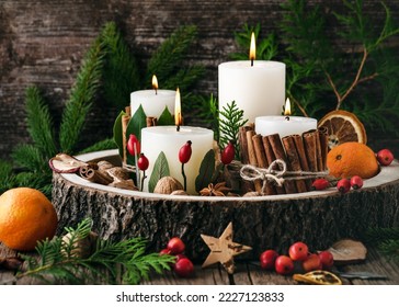 Christmas, advent wreath with four white burning candles decorated with natural material. Slices of fresh dried apple, orange and spices for cooking or baking. Rustic style. Handmade home decoration.