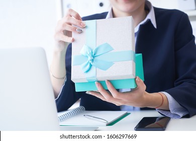 Christmas, any holiday. Office employee received a gift from her colleagues. Closeup woman hands holds gift box on office background. - Powered by Shutterstock