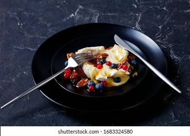 Christmas Appetizer Maple Pecan Baked Brie Cheese With Berries: Blueberries, Cranberries, And Honey On Top Served On A Black Plate With Silver Cutlery On A Dark Concrete Background, Horizontal View