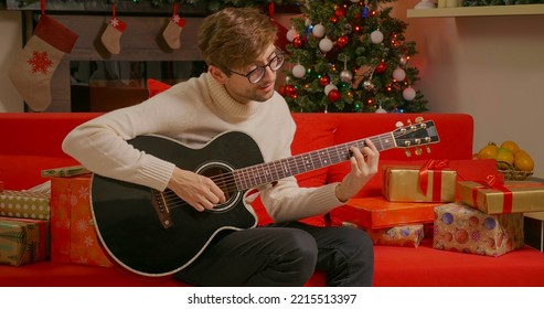 Christmas atmosphere. Smiling handsome man playing guitar singing Christmas songs sitting near a decorated home. All about winter holidays and Xmas. - Powered by Shutterstock