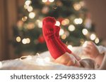 Christmas baby with red sock with Christmas tree decorations in the background, baby laying and showing cute little feet