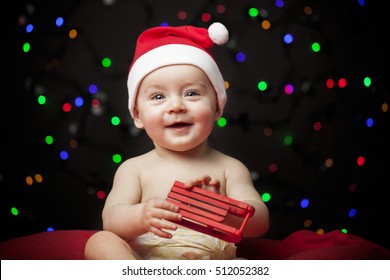 Christmas Baby In Santa Hat Holding A Sled Against Black Background