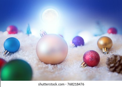 Christmas background with Christmas balls on snow over fir-tree, night sky and moon. Shallow depth of field.