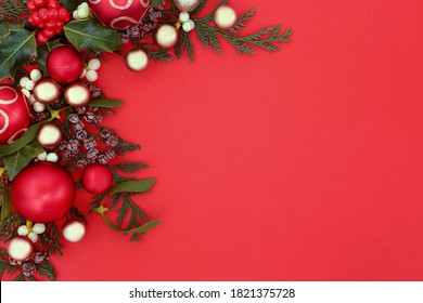 Christmas Background Border With Bauble Decorations, Holly & Winter Greenery Of Mistletoe, Ivy, & Cedar Cypress Fir On Red. Xmas New Year Composition For The Festive Season. Top View, Copy Space.