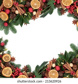Christmas Background Border With Cinnamon Spice, Dried Orange Fruit, Bauble Decorations, Holly And Winter Greenery Over White With Copy Space.