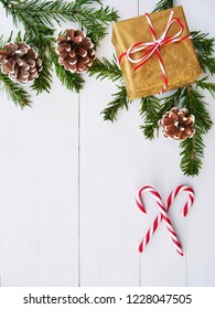 Christmas background with candy cane, gift, cones and fir branches over white wooden background.