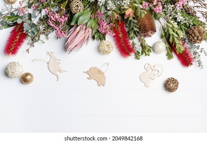 Christmas Background Decorated With Australian Native Wooden Animals And Flowers - Eucalyptus Leaves, Protea, Banksia, Callistemon, Tea Tree And Wax-flowers, On A Rustic White Background. 