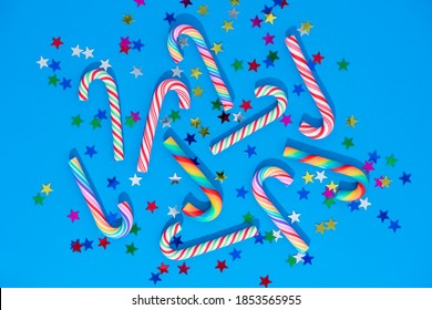 Christmas Background With Different Candy Cane And Star Confetti On Blue. Rainbow Candy Canes And Traditional Icicles. 