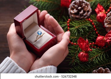 Christmas Background. Engagement Ring In Female Hands Among Christmas Decorations On Wood Background. Romance, Jewelry Concept - Woman Hands With Wedding Ring In Gift Box. Gift On Valentine's Day