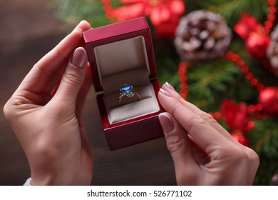 Christmas Background. Engagement Ring In Female Hands Among Christmas Decorations On Wood Background. Romance, Jewelry Concept - Woman Hands With Wedding Ring In Gift Box. Gift On Valentine's Day