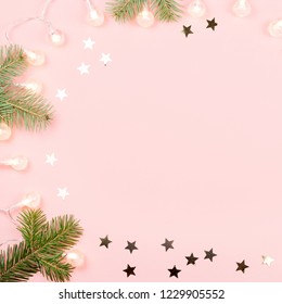 Christmas background with fir branches, Christmas lights and confetti on pink background. Copy space