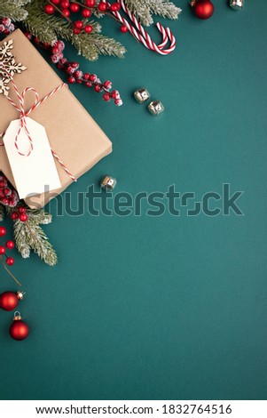 Christmas background with gift box and classic decorations. Fir branches, red balls, jingle bells on turquoise background. Gift box with tag.