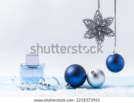 Christmas background, silver ribbon and blue and silver balls, star and artificial snow and glass perfume bottle on a light background. New Year or Christmas present.