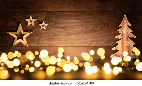 Christmas background with wooden ornaments arranged on a dark wood board and bokeh lights shining in the foreground