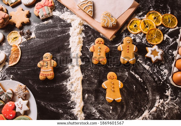 Christmas bakery. Conceptual\
pastry collection. Gender diversity. Festive decorated gingerbread\
icing woman dividing from biscuit figures man by flour line on\
black desk.