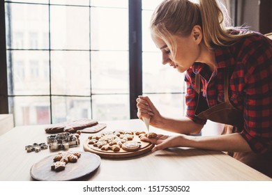 Christmas bakery. Woman decorating Christmas gingerbread cookies with sugar icing. Festive food, cooking process, family culinary, Christmas and New Year traditions concept