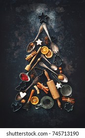 Christmas baking background with fir tree made from kitchen utensils, cookies, spices, cinnamon sticks, anise stars on rustic baking tray, top view