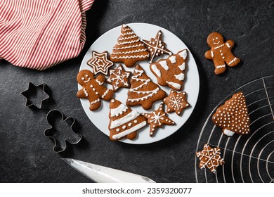 christmas baking, cooking and food concept - close up of iced gingerbread cookies on plate, molds, towel and pastry bag on black table top - Powered by Shutterstock