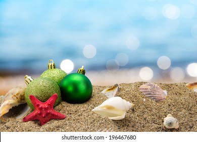 Christmas balls and shells on sand with summer sea background 