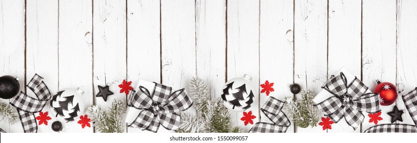 Christmas banner of black and white checked buffalo plaid ribbon, gifts and ornaments. Above view long bottom border on a white wood background.
